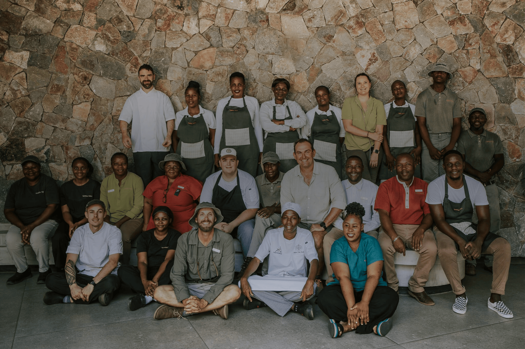 The Tanda Tula hosts standing together in the bush, smiling and warmly welcoming guests.