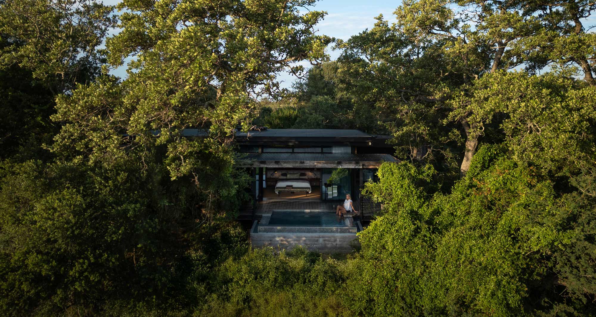 Exterior of a Tanda Tula Safari Suite nestled in the bush with river views and surrounding trees.