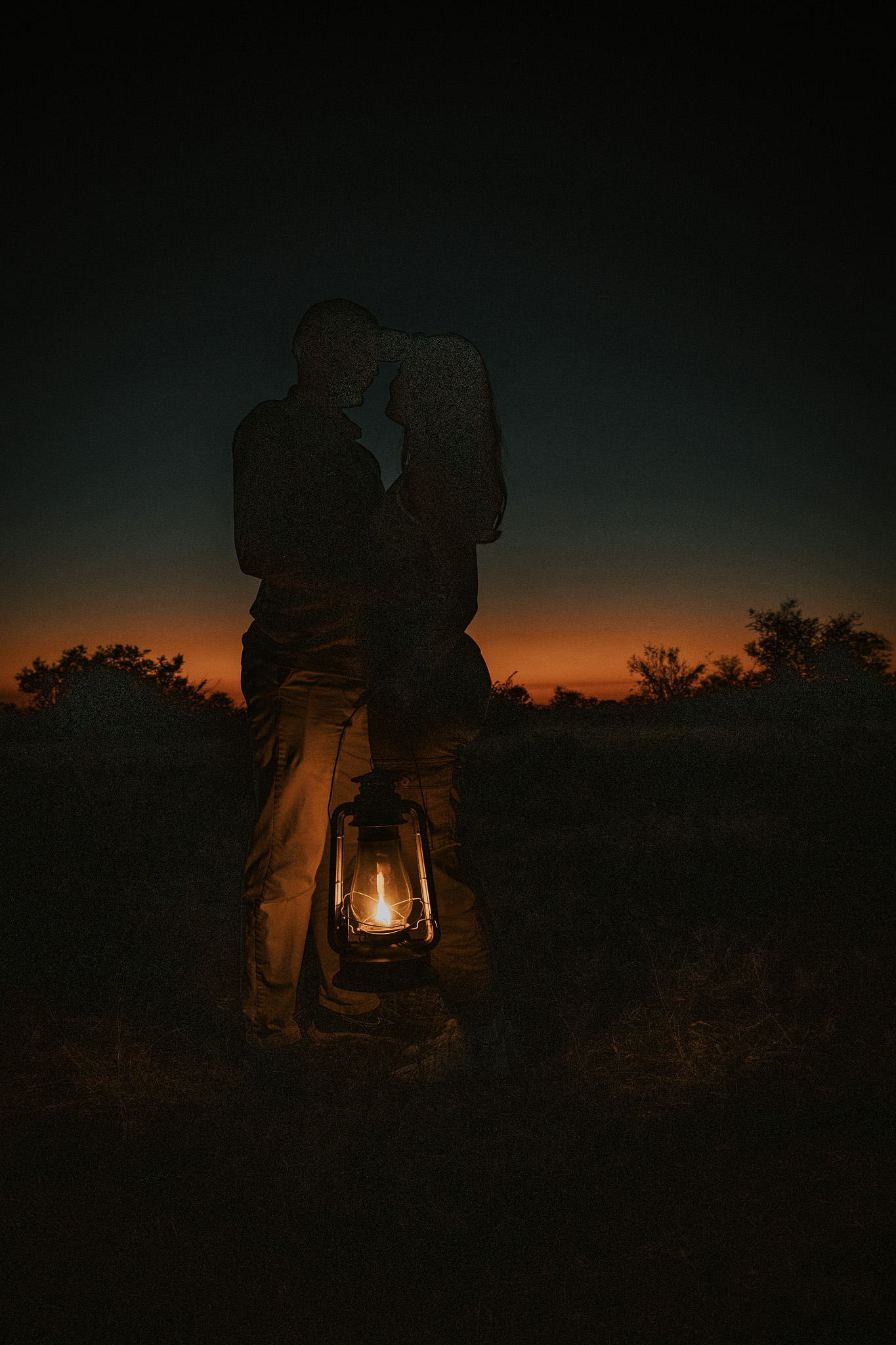 Couple sharing a kiss at sunset while holding a lantern.