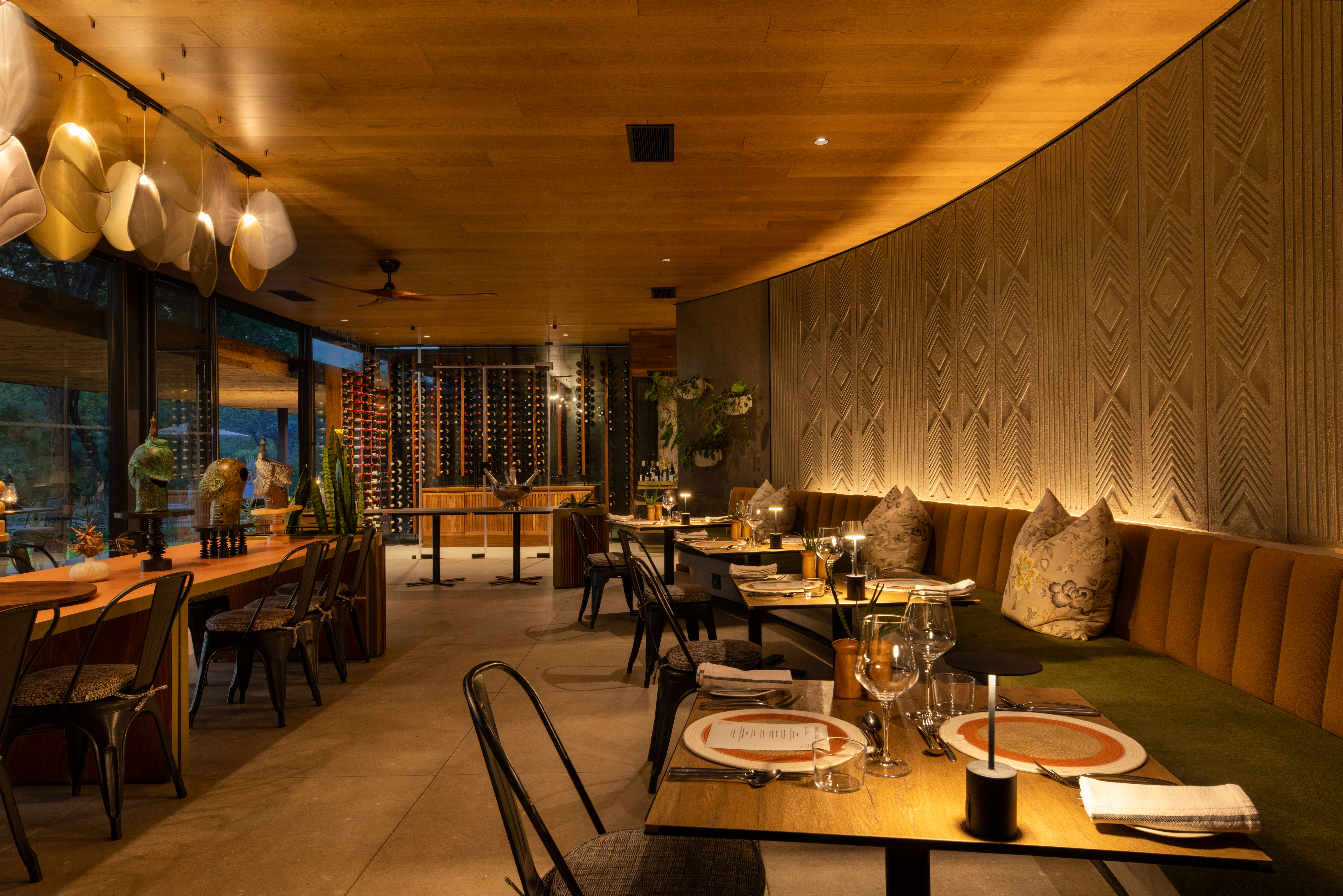 An elegant interior dining space at Tanda Tula featuring soft lighting, warm tones, handcrafted wall textures, wine displays, and beautifully set tables that reflect a refined, intimate safari atmosphere.