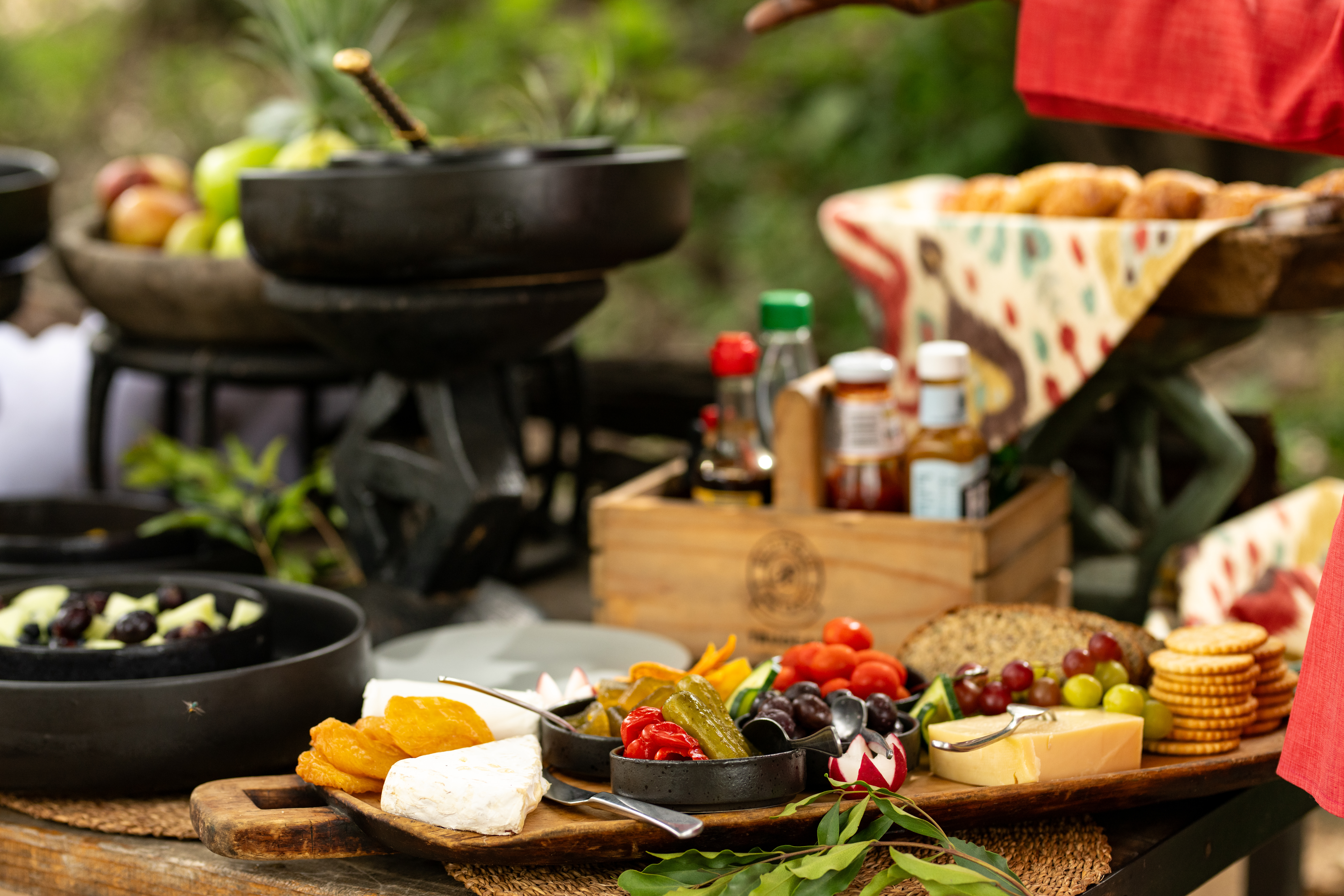 A colourful bush breakfast platter at Tanda Tula featuring cheeses, fresh grapes, crackers, dried fruit, pickled vegetables, and condiments, artfully arranged on rustic wooden boards outdoors in the Timbavati.