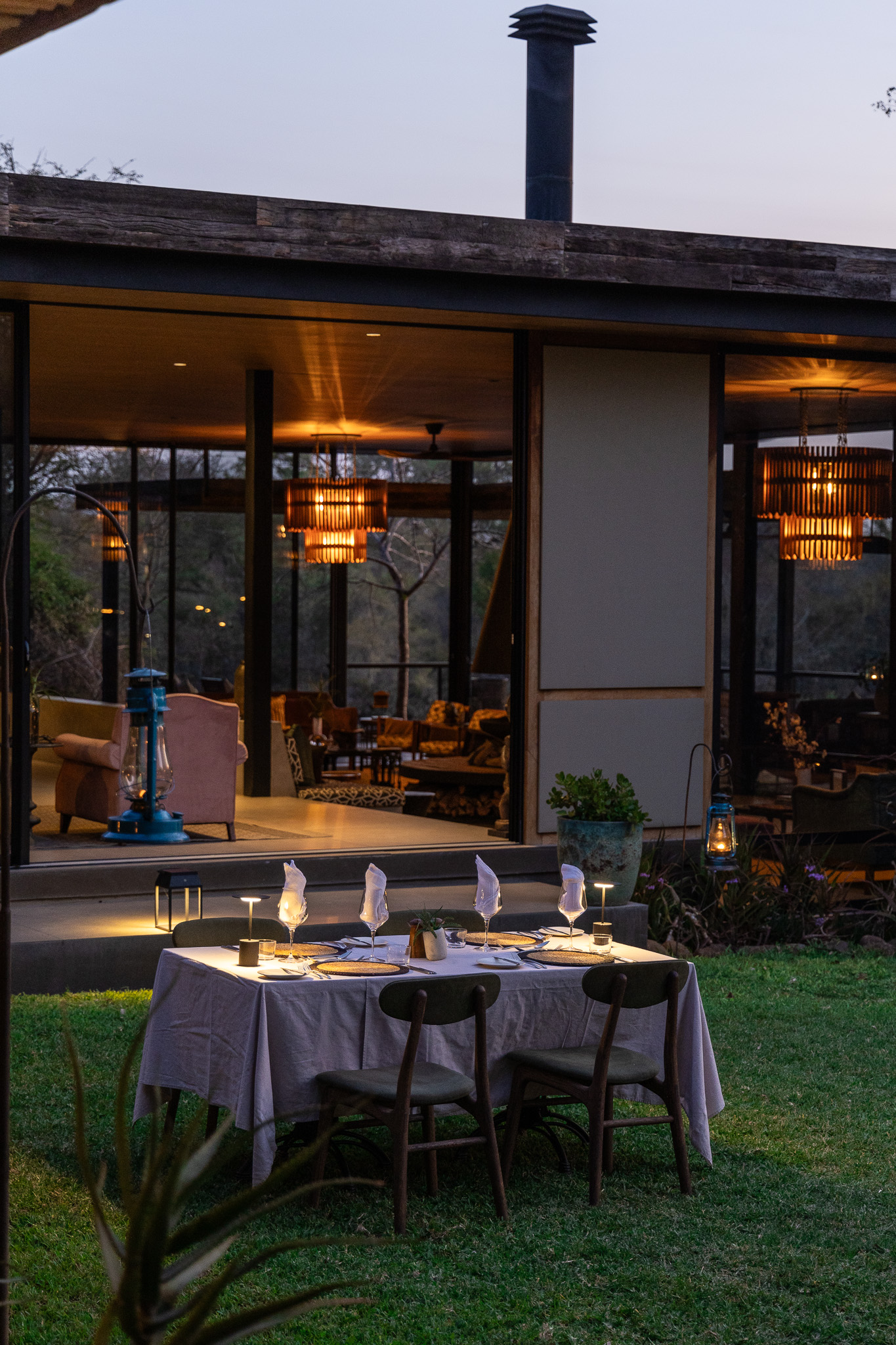 Candlelit dinner table set outside the lodge with warm interior lights glowing.